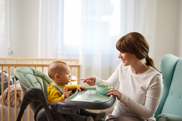 Mother spoon feeding her baby son at home