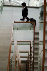 Top view of businessman with luggage moving down the stairs of modern office building