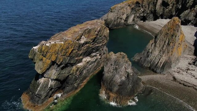 Trefor Sea Stacks aerial orbiting view of rocky columns with cormorants against a backdrop of Welsh mountains