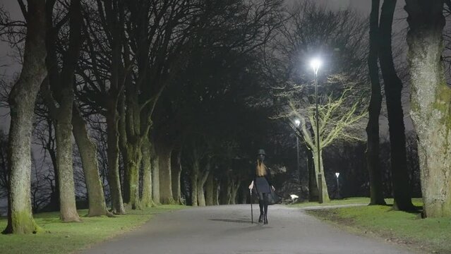 A young female child dressed for Halloween as a plague Doctor walks in between trees at night