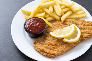 Wiener schnitzel with fried potatoes on black slate surface.typical vienna food