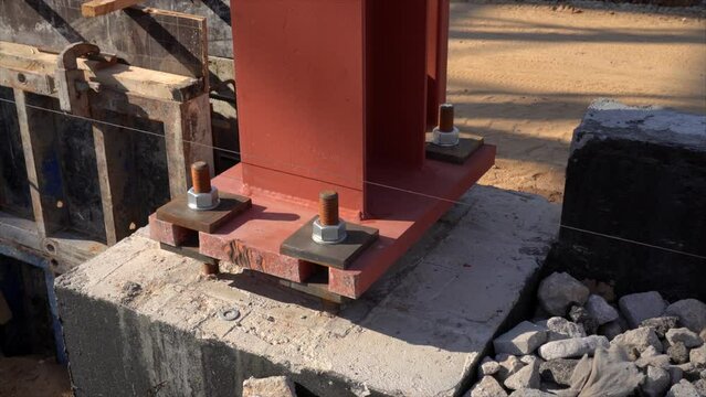 Metal supporting column mounted on the base pedestal  with huge nuts on screw rods on a building site.