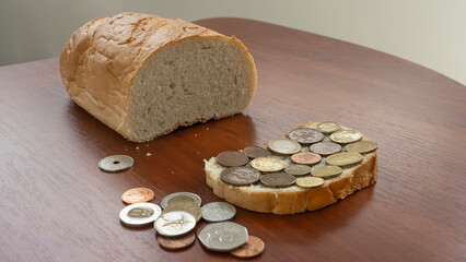 A loaf of white bread, a coin sandwich and a few coins on a brown table, the concept of a global food crisis, rising food prices, higher taxes