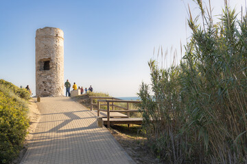 Fototapeta na wymiar Torre vigía en una playa de Cádiz en San Fernando al atardecer con cielo despejado azul, con grupo de gente contemplando atardecer.