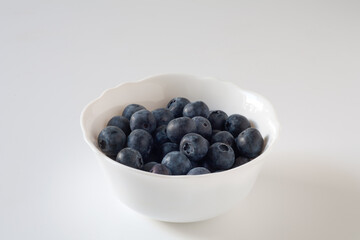 Blueberries are on the table in a white plate. On a white background.