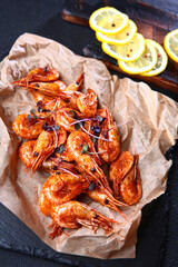 Grilled prawns on paper with lemon and spices on vintage dark background, top view, copy space. Seafood dinner.Appetizer for beer.