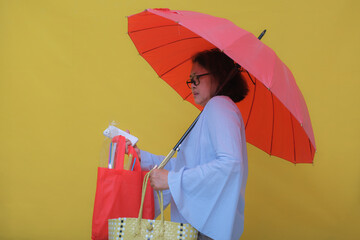 Side view: A middle-aged woman holding a smartphone and a red shopping bag under a red umbrella.