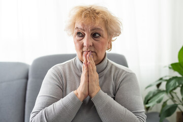 Frowning upset mature woman put head on folded hands, looking in distance. Lost in thoughts upset woman sitting alone, head shot close up portrait. Mental disorder or dementia, health problem concept