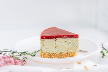 Pistachio cheesecake on plate against white background with dried flowers.
