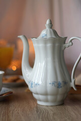 Cup of tea or coffee, plate of cookies, cup of blueberries, plate of chocolate, glass of juice, book, reading glasses, teapot, flowers and lit candles on the table. Brunch or afternoon tea concept.