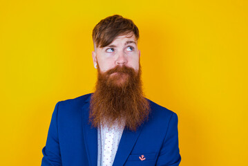red haired man wearing blue suit over yellow studio background making grimace and crazy face,...