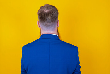 The back view of a Red haired man wearing blue suit over yellow studio background. Studio Shoot.
