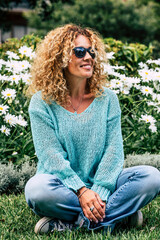 One woman enjoying outdoor park sitting on the grass and smiling. Springtime and happy people. Casual female smile and relax in the nature. Daisies in background. Spring season. Freedom and happiness