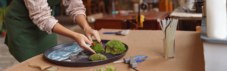 Woman decorator making green ikebana on tray with epoxy resin in florist workshop