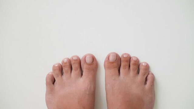 First person top view 4k stock video footage of two female pedicured feet isolated on white empty background with copyspace. Female toenails painted with pink natural look color lacquer