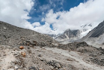 Rocky terrain against snowy mountains covered with clouds and a blue sky - Powered by Adobe