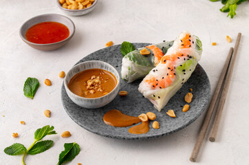 Fototapeta na wymiar Summer rolls with fresh vegetables and shrimps and peanut sauce. Vietnamese appetizer. Salad spring rolls with prawns. Healthy food concept