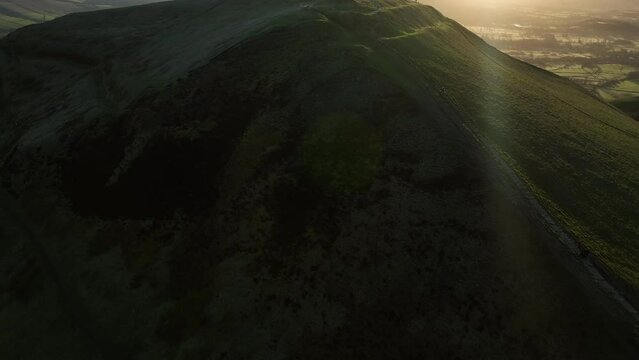 Dramatic aerial tilt up reveal establishing shot of people stood at Mam Tor trig point enjoying the views and sunrise with lens flares.