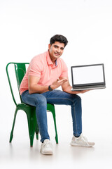 Young indian man sitting on chair and showing laptop screen.