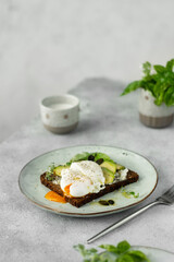 Healthy Breakfast with Bread Toast and Poached Egg with Avocado and cream cheese on a light grey background.