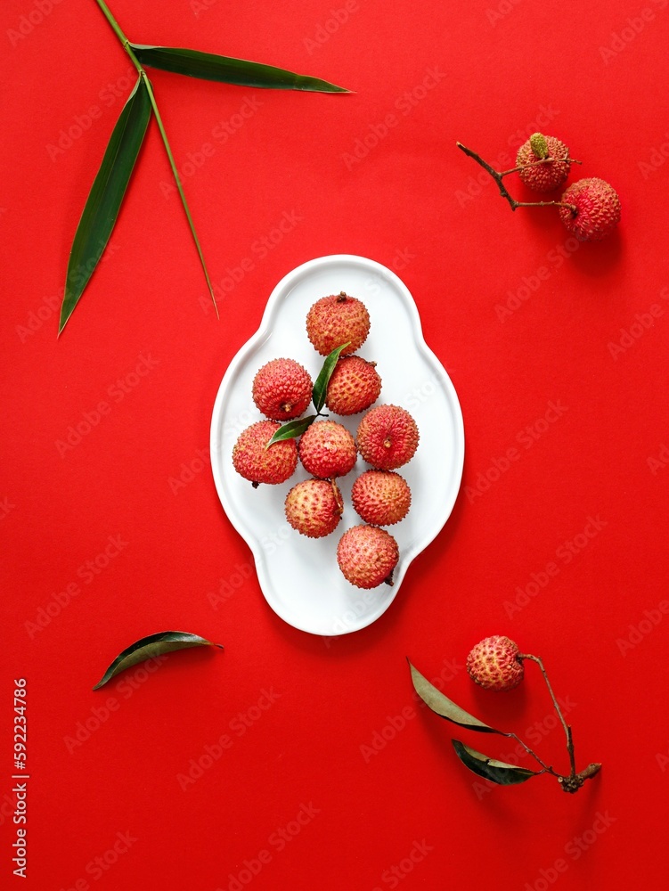 Poster top view of lychee tropical fruit on a white plate on a red surface