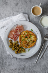 Homemade tortilla - Traditional  Spanish Omelette with potato in a plate on a grey background. Served with bacon and olives.