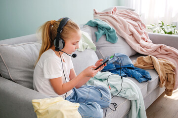 A girl is playing on a mobile phone. The room is a mess. The child scattered things in the room.