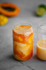 Tropical summer smoothie on a light background. Drink Lassi made of yogurt, papaya, mango, other tropical fruits, spices and ice. Close-up.