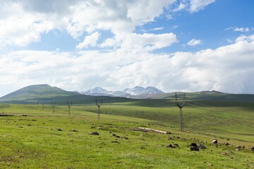 Green valley view with a spiral of power lines Aragats mountain stuck into white clouds  background