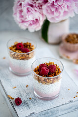 	
Raspberry chia seed parfait made with granola and berries in a cups with peony flowers on the background.