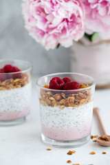	
Raspberry chia seed parfait made with granola and berries in a cups with peony flowers on the background.