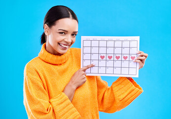 Health, portrait and female with a calendar in a studio to track her menstrual or ovulation cycle. Happy, smile and face of a woman model pointing to a paper period chart isolated by blue background.