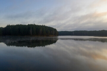 Fototapeta premium Drone photography of lake, lakeside and fog and fishing man in a boat during summer sunset.