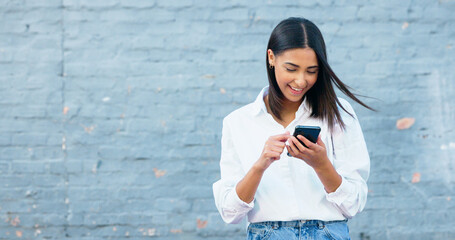 Happy young woman texting on a phone and laughing in the city. Cheerful female smiling while...