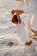 A little girl, a child enters the water with foam on the seashore. Mom holds the child by the hands. Girls in white dresses