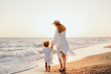 A young girl, mother, with a little daughter in white dresses, walk on the water on the seashore at sunset.