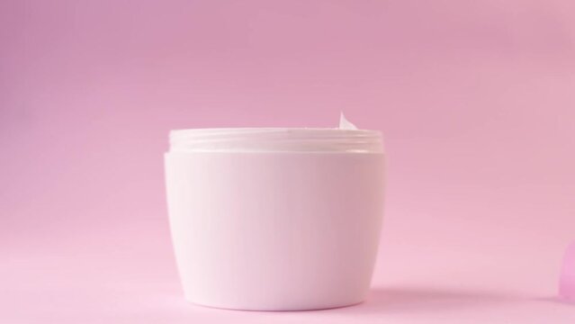 Closeup shot of a hand opening a container of skin cream on a pink background