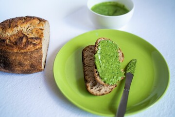 Green pesto sauce on the toast and sourdough bread loaf, close-up