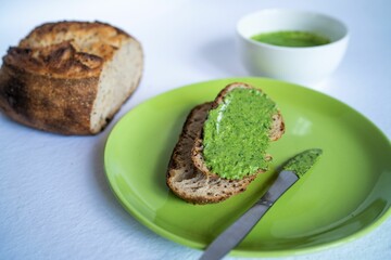 Green pesto sauce on the toast and sourdough bread loaf, close-up