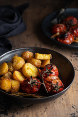 Roasted potatoes and tomatoes in a black plate. Rustic food.