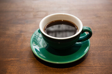 Half top view of green and white coffee mug with coffee on a brown wooden table.