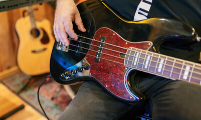 Crop male musician playing bass guitar near synthesizer in studio