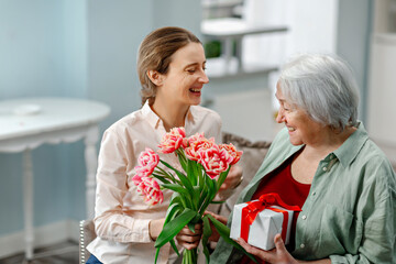 Happy Mother's Day. The daughter congratulates her mother and gives her flowers and a gift.
