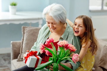 A smiling caring granddaughter presents flowers to an elderly grandmother on women's Day.