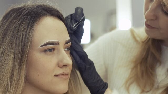 Portrait of a young woman whose eyebrows are plucked with tweezers in a beauty salon, she talks with the master during the procedure. beauty industry.