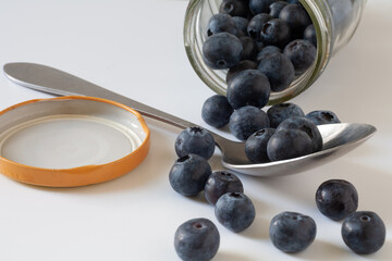 There are scattered blueberries on the table. Near it is a jar, a spoon, a lid.