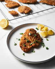 Baked Chicken Schnitzel on white plate with lemon. Rack or grid with baked schnitzel in breadcrumbs...