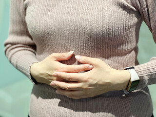 胸の下を両手で押さえる女性