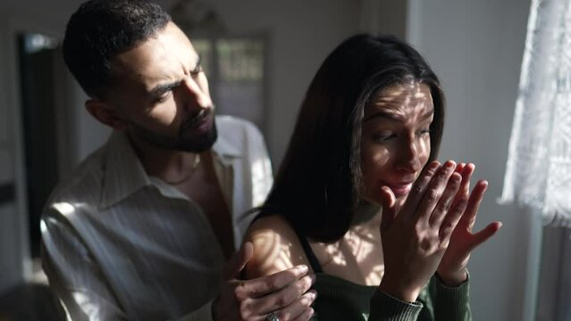 An Arab Boyfriend comforting sad tearful girlfriend standing by window with sunlight shining through curtains. Empathic and supportive couple during difficult times