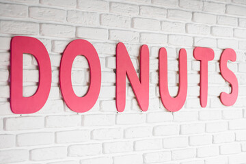 The word donuts on a white wall in a cafe, interior decor in a cafe with donuts, close-up lettering.